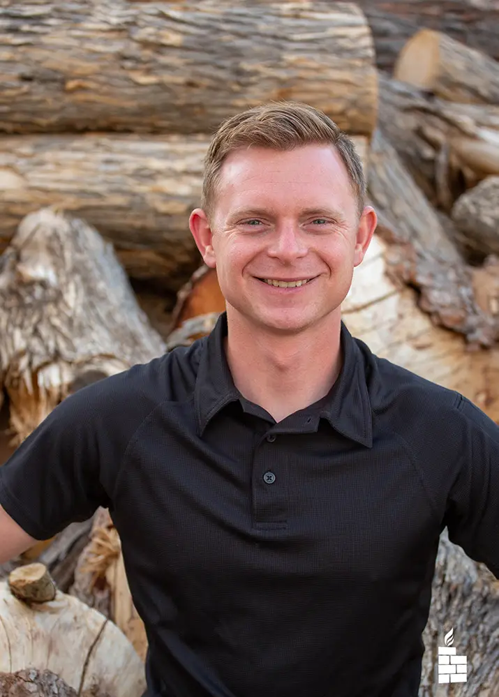 Portrait of handsome young man in a black collared shirt. Firewood stacked in the background.